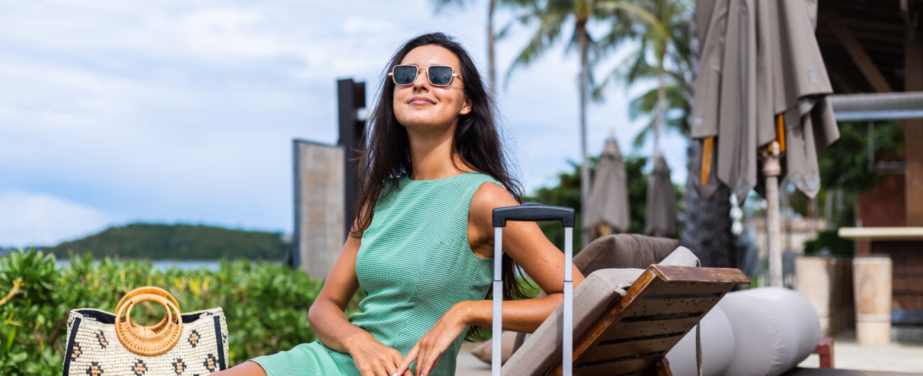 happy-caucasian-pretty-long-hair-elegant-tourist-woman-dress-with-red-suitcase-outside-hotel